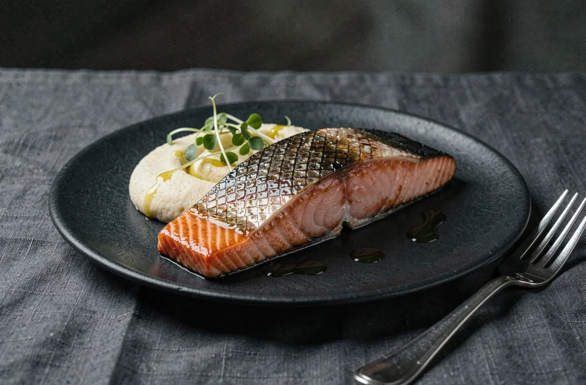 Dressage gastronomique de saumon à basse température avec peau ultra-croustillante sur ardoise noire, purée de chou-fleur et herbes fraîches